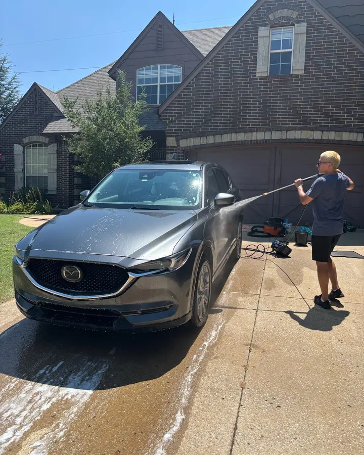 Sam rinsing a gray Mazda CX-5 in a customer's driveway